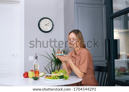 Blogger young woman uses smartphone for taking photos of vegetables lying on kitchen table. Concept of social networks. Concept of healthy eating.