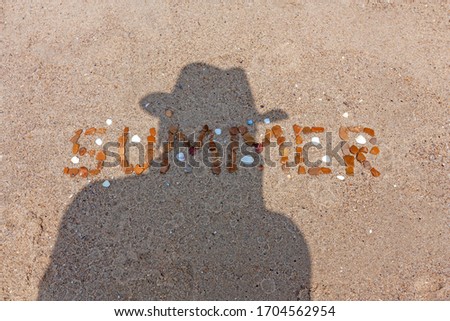 On the sand of the beach, the word "summer" is stoned, and the shadow of the photographer in the cowboy hat is also visible.