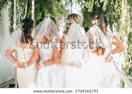 Hen party evening party. Girls in white dresses holding from back, white flowers on their hands. Celebrating bride and girlfriend with wreaths and veil. The day before the wedding.