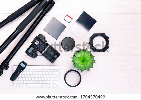Top view of photographer workplace with dslr camera, lens and camera accessories on white wooden table with copy space for text. Camera, photography, audiovisual content concept.  Royalty-Free Stock Photo #1704570499
