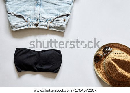 Flat lay picture of summer clothes, isolated on white background. Straw hat, sunglasses, black top and light blue jeans shorts. Summer vacation background.
