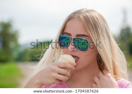 Beautiful girl, has blue sunglasses, blonde white long hair, happy face. Eating ice cream.  Summer fashion style. Nature and food people portrait. Romantic pure makeup. Close up.