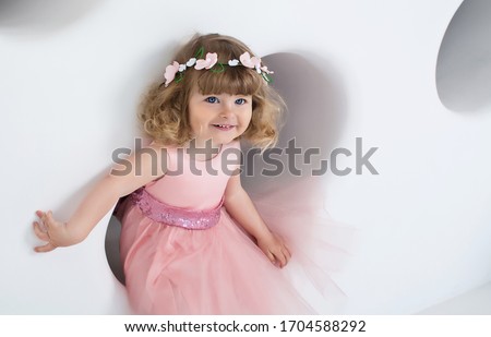 little girl in pink dress smiles in white room	 Royalty-Free Stock Photo #1704588292