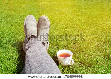 Female legs on green grass and cup of tea. Rest concept.