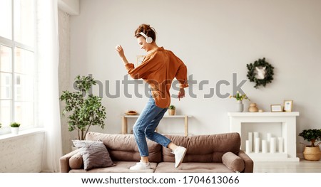 Positive young lady in wireless headphones and casual clothes listening to music with pleasure and dancing of sofa in light modern living room
 Royalty-Free Stock Photo #1704613066