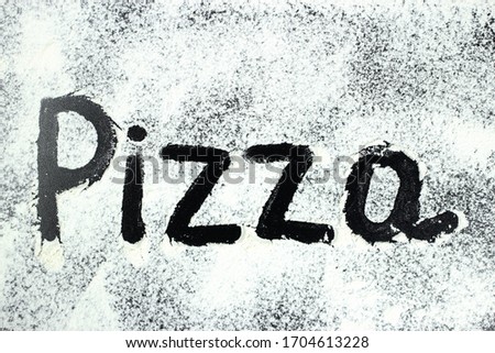 The word pizza is drawn with finger on flour, white powder