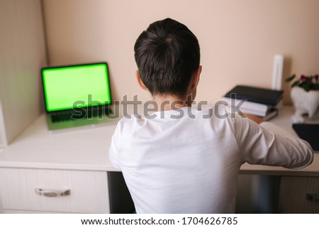 Schoolboy study at desk in his room. Boy use laptop and writing in notebook. Books and tablet on the table. Study home during qurantine. Green screen