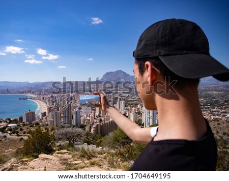 
young man taking a photo of the city of benidorm with his smartphone