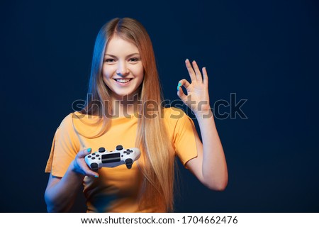 Gamer girl. Happy girl holding video game joystick showing OK sign, on blue background