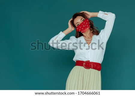 stylish young woman in red mask touching hair isolated on blue
