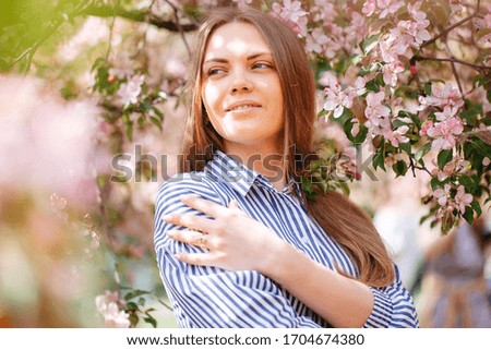 Young happy woman on a background of pink flowers in the garden. The girl in the dress stands on the background of sakura.