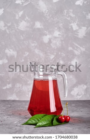 Fresh cherry lemonade in jug on gray table background, copy space. Cold summer drink. Berry cocktail