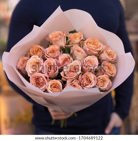 Young man with a gift bouquet of fine peach roses, mono bouquet of roses. Peony roses flowers. Young man holding fresh bouquet of peony roses.