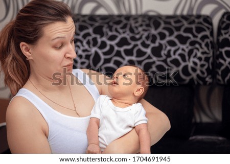 A young mother looks at her newborn baby in surprise. Woman holds a baby