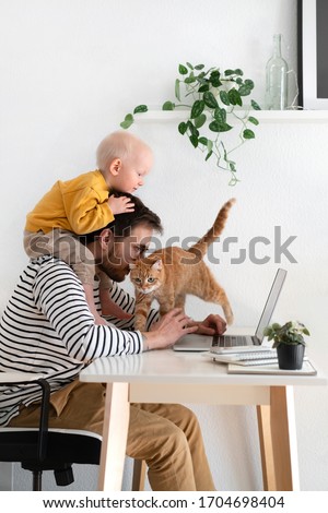 Working from home. Father freelancer with baby and cat in home office at his desk. Family indoors Royalty-Free Stock Photo #1704698404