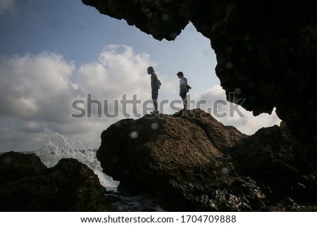 
two boys stand on a rock and look at a storm at sea