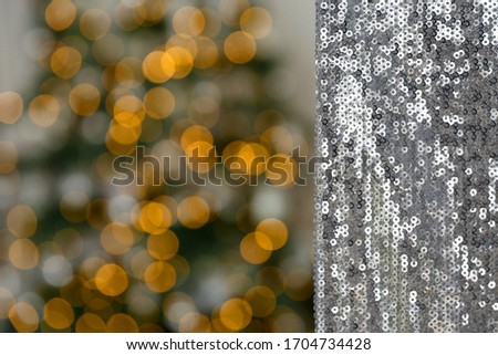 Christmas, New Year background and texture. Material or fabric embroidered with glaring silver sequins on a background of bokeh of yellow garland lights