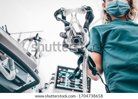 COVID19 / 2019-ncov concept: Nurse applies a mask of the mechanical ventilation machine, which can be seen in the foreground. therapy used for lung breathing, in intensive care. Royalty-Free Stock Photo #1704738658