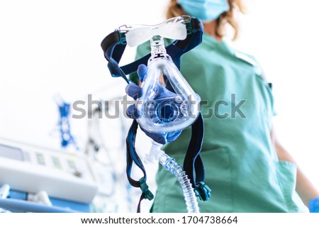 COVID19 / 2019-ncov concept: Nurse applies a mask of the mechanical ventilation machine, which can be seen in the foreground. therapy used for lung breathing, in intensive care. Royalty-Free Stock Photo #1704738664