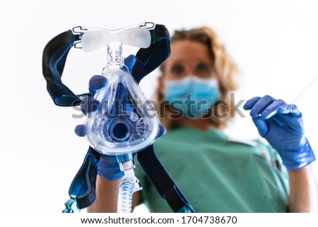 COVID19 / 2019-ncov concept: Nurse applies a mask of the mechanical ventilation machine, which can be seen in the foreground. therapy used for lung breathing, in intensive care. Royalty-Free Stock Photo #1704738670
