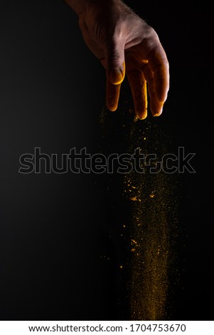Strong man hand sprinkling and scattering yellow turmeric which is famous eastern seasoning on dark background with strong light with his fingers and palm making amazing nice dust