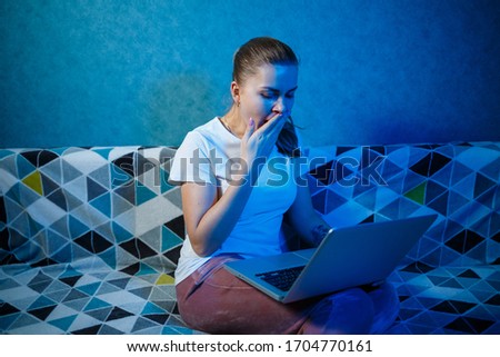 A girl in a white T-shirt is sitting at home on the couch with a laptop on her lap and looking at the screen. Reads new important information. Search News