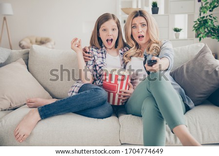 Photo of pretty blond lady mom daughter sit sofa hugging eat popcorn switch on tv set watch movie open mouth intrigue moment stay home quarantine together best friends living room indoor