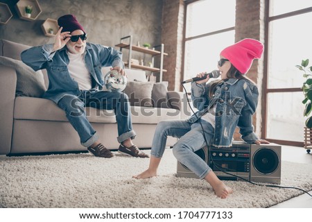Photo of two people grandpa listen little granddaughter sing mic old fashion song cool style specs denim outfit hat house party sit tape player recorder stay home quarantine indoors