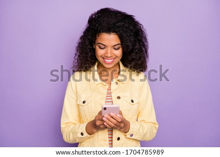 Portrait of positive cheerful afro american girl using her smartphone reading social network news chatting with friends wear casual clothing isolated violet color background