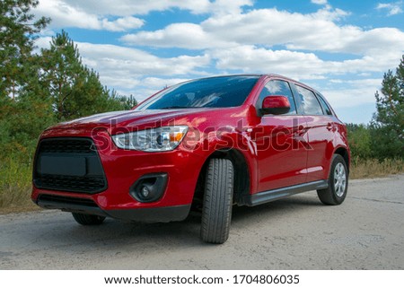 Beautiful red car on road in forest in background. Royalty-Free Stock Photo #1704806035