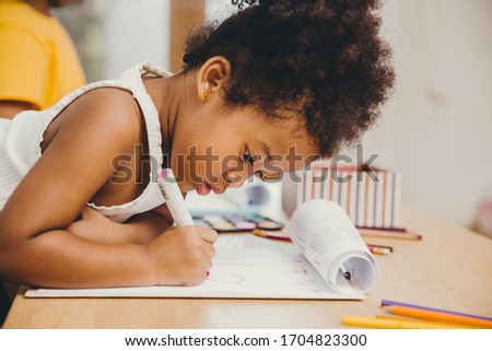 Closeup little child girl black skin writing doing homework at home.
