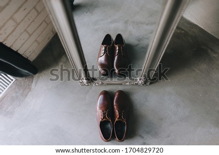 Stylish men's brown shoes stand opposite a modern mirror and are reflected. Photography, concept.
