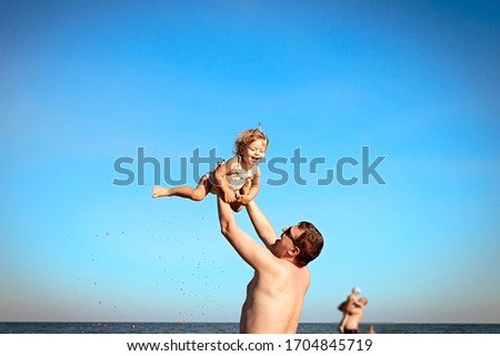 
happy little girl in a swimsuit flies in the sky, dad throws up his daughter and catches her. Background of blue sky. Sea, vacation and travel. Father's day. Daughter's day. Family day.