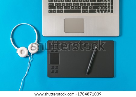 White headphones, laptop and graphic tablet on a blue background. A device for working in image editors.