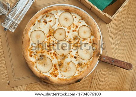 Appetizing baked pizza with white sauce, pear, and gorgonzola cheese with crisp on a wooden background. Restaurant table setting. Top view