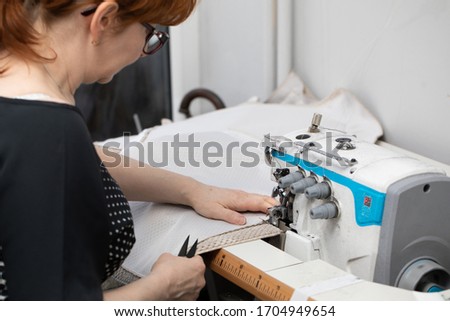 Experienced seamstress sews pillow covers on a sewing machine called overlock. Royalty-Free Stock Photo #1704949654
