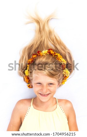 Close up portrait of lovely little girl lying against white background with long hair with arranged yellow and orange marigold flowers