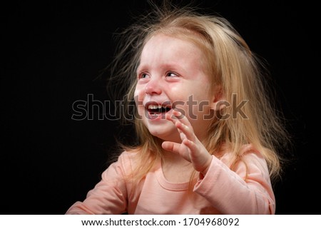Portrait of a crying blond baby girl on black background