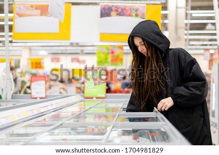 girl with dreadlocks chooses products in the supermarket refrigerator