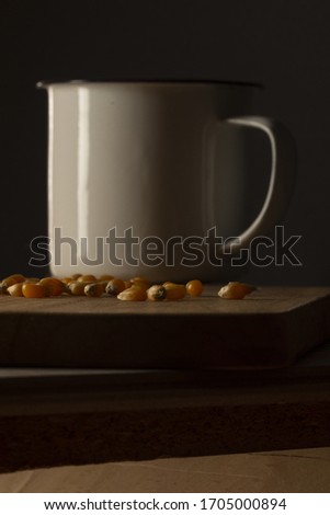Still life with corn kernels on a wooden table with a white metal mug, dark food.