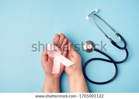 female hand holds a pink bow-shaped ribbon on a blue background. Breast cancer awareness campaign concept.
