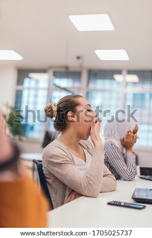 Portrait of a tired businesswoman yawning while having a business meeting in the office. Royalty-Free Stock Photo #1705025737