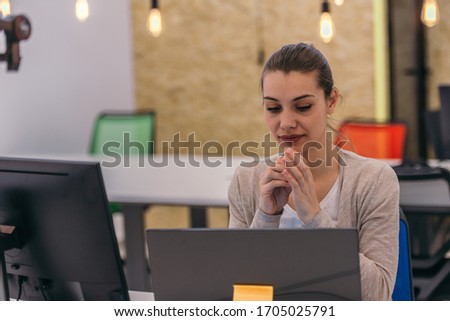 An attractive businesswoman working on a computer and talking with her colleagues in the office.