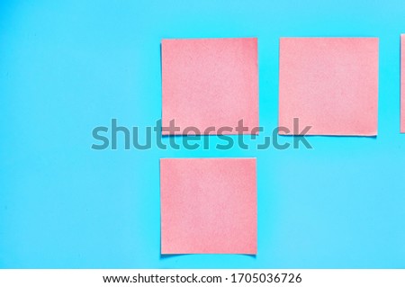 Frame of many pink square blank paper stickers on blue background. Copy space. Top view