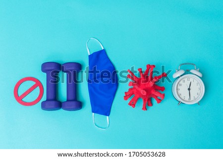 Two dumbbells of blue color, coronavirus, block sign, alarm clock and mask on a light blue background. Pandemic and quarantine concept.