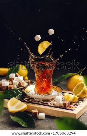 Black tea splash in armudu glass with lemons and sugar cubes Royalty-Free Stock Photo #1705063294