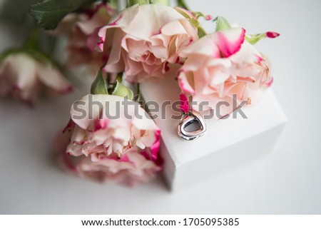 Top view picture of the white gold jewellery heart-shaped bead placed on the top of the white square box with tender blush pink blossoms on the background