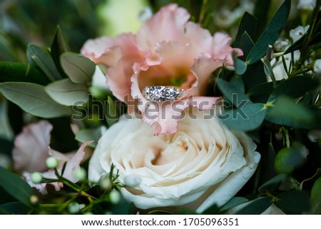 Close up picture of the vintage white and yellow gold engagement ring with round diamond placed inside coral flower, cream color rose and dark green leaves on the background