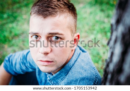Portrait of a pensive young guy in a blue denim shirt on the nature.