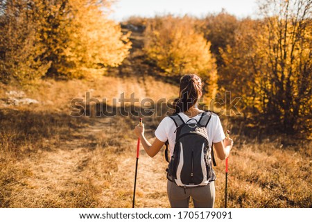 Back view of woman with backpack and trekking sticks. Nordic walking. and hiking. Autumn nature around and path forward. Travel concept. Royalty-Free Stock Photo #1705179091